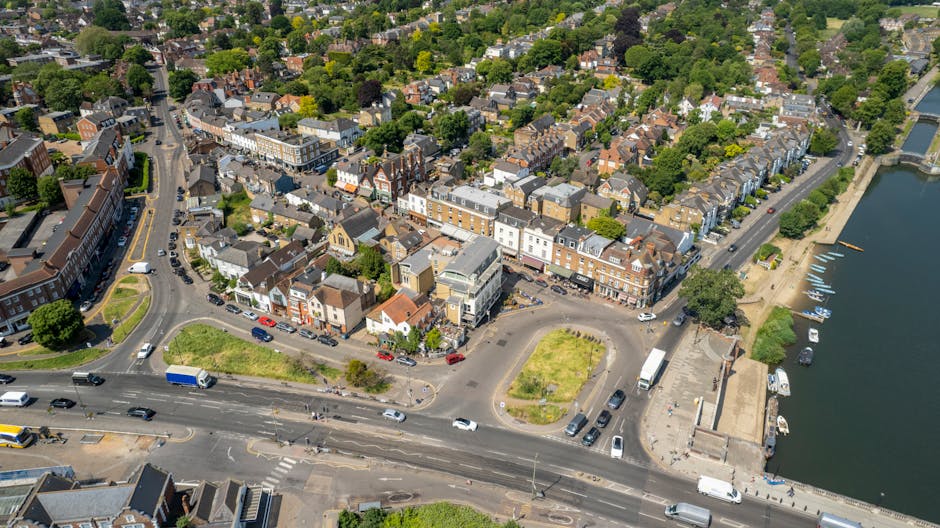 Aerial view of Uxbridge town centre showing a mix of residential and commercial buildings along High Street, with narrow streets and a nearby waterway. The scene includes parked cars, moving vehicles 
